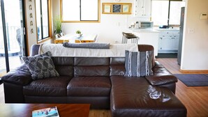 A modern living room with a brown leather sofa, a dining table, and a kitchen in the background.