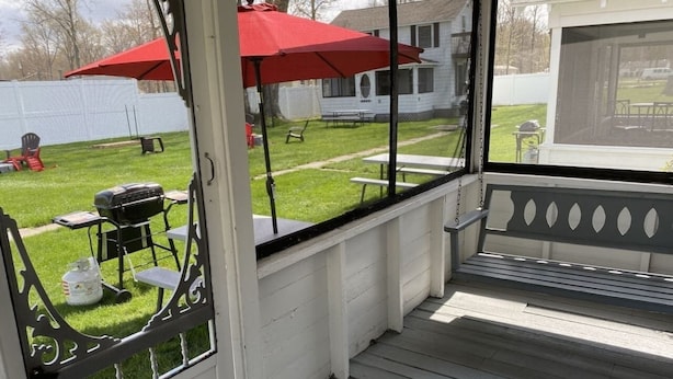 En overdækket terrasse med bænk, grill og røde parasoller.