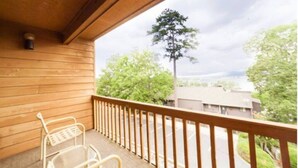 Un balcone in legno con una sedia in metallo e vista su alberi ed edifici.