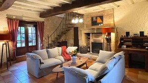 Un salon chaleureux avec deux canapés, une table basse et une cheminée. Un escalier mène à l’étage supérieur.
