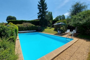 A rectangular swimming pool with a tiled edge, surrounded by a gravel area. There are two white lounge chairs and a green umbrella. - Rent Charming house in Dordogne with swimming pool (Lanquais)