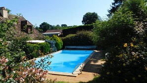 Une piscine rectangulaire avec un escalier, entourée d’une végétation luxuriante et avec une maison en arrière-plan.