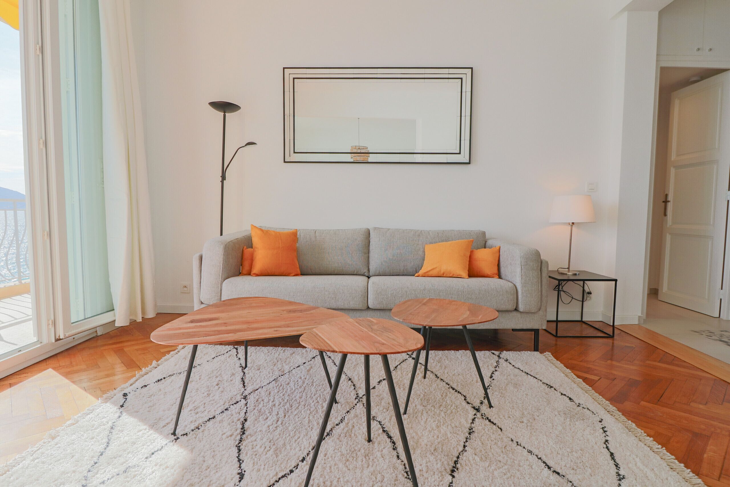 A living room with a grey sofa, orange cushions, two wooden side tables, and a large framed mirror on the wall.