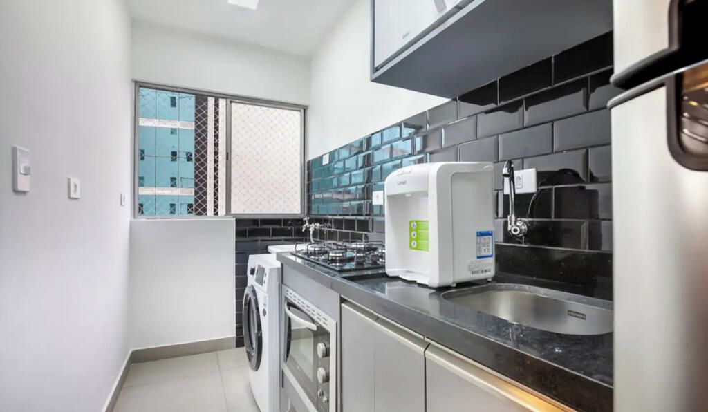 A compact kitchen with a washing machine, a built-in oven, a coffee maker, and a stainless steel sink.