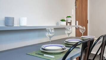 A dining table set with plates and wine glasses, a green placemat, and a small potted plant on a white shelf.