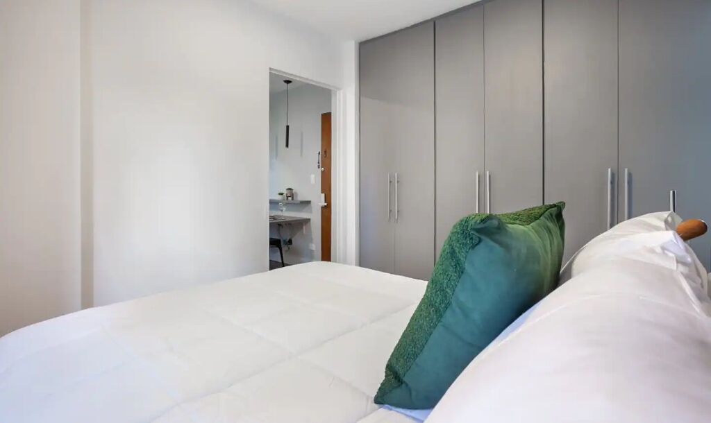 A bedroom with a bed, a green pillow, and grey wardrobe.