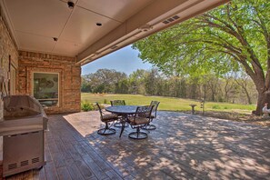 A covered patio with a grill, outdoor table, and chairs, overlooking a grassy area with trees. - 16-Acre Pilot Point Ranch: Private Pond (Pilot Point)