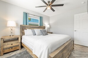 Une chambre à coucher avec un lit en bois, deux tables de chevet avec des lampes, un ventilateur de plafond et une porte.