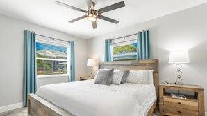 Ein Schlafzimmer mit einem Holzbett, einem Deckenventilator, zwei Nachttischen mit Lampen und einem Fenster mit Vorhängen.
