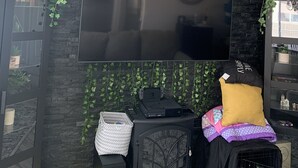 A living room with a flat-screen TV mounted on a black brick wall, a black wood-burning stove, and a black bookshelf with decorative items. - Coming soon (North Las Vegas)