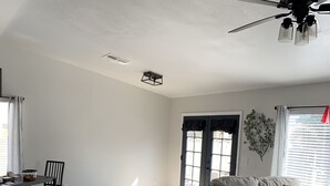 A living room with a sofa, a dining table, and chairs. There is a ceiling fan and a window with blinds. - Coming soon (North Las Vegas)