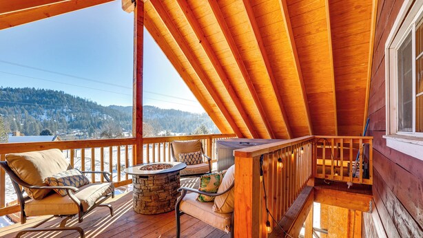A wooden deck with a stone fire pit, two cushioned chairs, and a view of a snowy landscape.