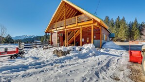 A wooden cabin with a balcony, surrounded by snow and mountains in the background.