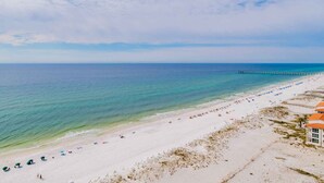 En strand med en brygga som sträcker sig ut i havet, vit sand och kristallklart blått vatten.