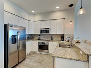 A modern kitchen with white cabinets, stainless steel appliances, granite countertops, and pendant lighting. - Penthouse Views, Resort Amenities, and Luxe Furnishings! Book Today! (Pensacola Beach)