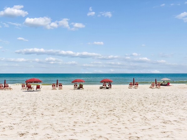 A beach with rows of sun loungers and umbrellas, a clear sky, and the ocean in the background. - Ocean Breeze West #204 | Unbelievable Beach Views! (Perdido Key)