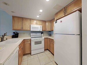A compact kitchen with wooden cabinets, a white refrigerator, a microwave, a stove, and a coffee maker.