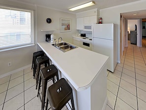 Een moderne keuken met een centraal eiland, barkrukken, een spoelbak, een fornuis en een koelkast.