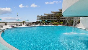 A swimming pool with lounge chairs and umbrellas, surrounded by a multi-story building. - Edgewater #1205 | Gulf Front in Destin, Spectacular Views + Amenities (Miramar Beach)