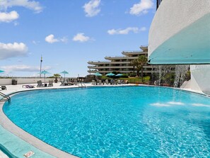 Una piscina con lettini e ombrelloni, circondata da un edificio a più piani.