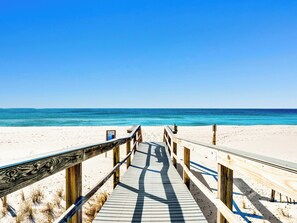 Une promenade en bois qui mène à une plage aux eaux d’un bleu limpide.