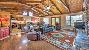 A spacious living area with a high ceiling, leather furniture, a kitchen in the background, and a stone fireplace. - Alto Cabin w/ Stunning Views, Hot Tub + Sauna! (Alto)