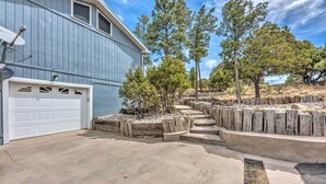 A residential property with a garage, a concrete driveway, and a landscaped area with trees and wooden planters. - Alto Cabin w/ Stunning Views, Hot Tub + Sauna! (Alto)