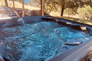 A hot tub with water bubbling, surrounded by lounge chairs and a wooden fence. - Alto Cabin w/ Stunning Views, Hot Tub + Sauna! (Alto)