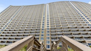 A high-rise building with a grid of balconies, a central stairwell, and a wooden viewing platform. - Relax in Style | Gulf-View 1BR Condo at Emerald Beach | Summer Specials (Panama City Beach)