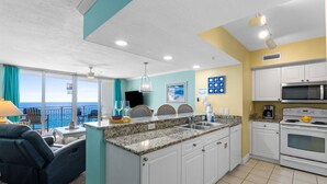 A modern kitchen with white cabinets, a granite countertop, and a view of the ocean. - Relax in Style | Gulf-View 1BR Condo at Emerald Beach | Summer Specials (Panama City Beach)