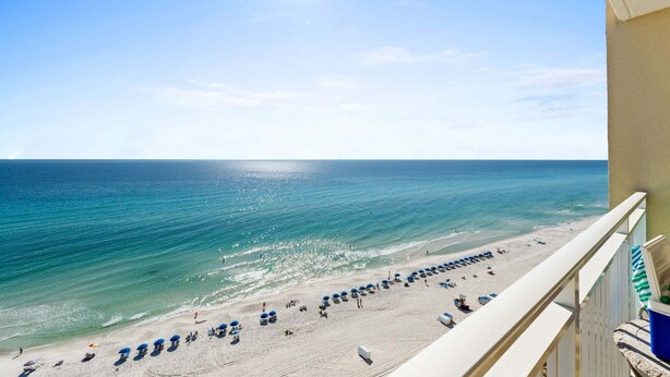 A beach view from a balcony with a clear sky, ocean, and beach umbrellas. - Relax in Style | Gulf-View 1BR Condo at Emerald Beach | Summer Specials (Panama City Beach)