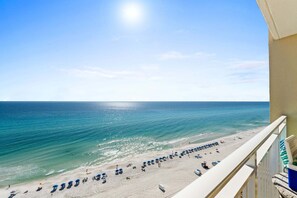 A beach view from a balcony with a clear sky, ocean, and beach umbrellas.