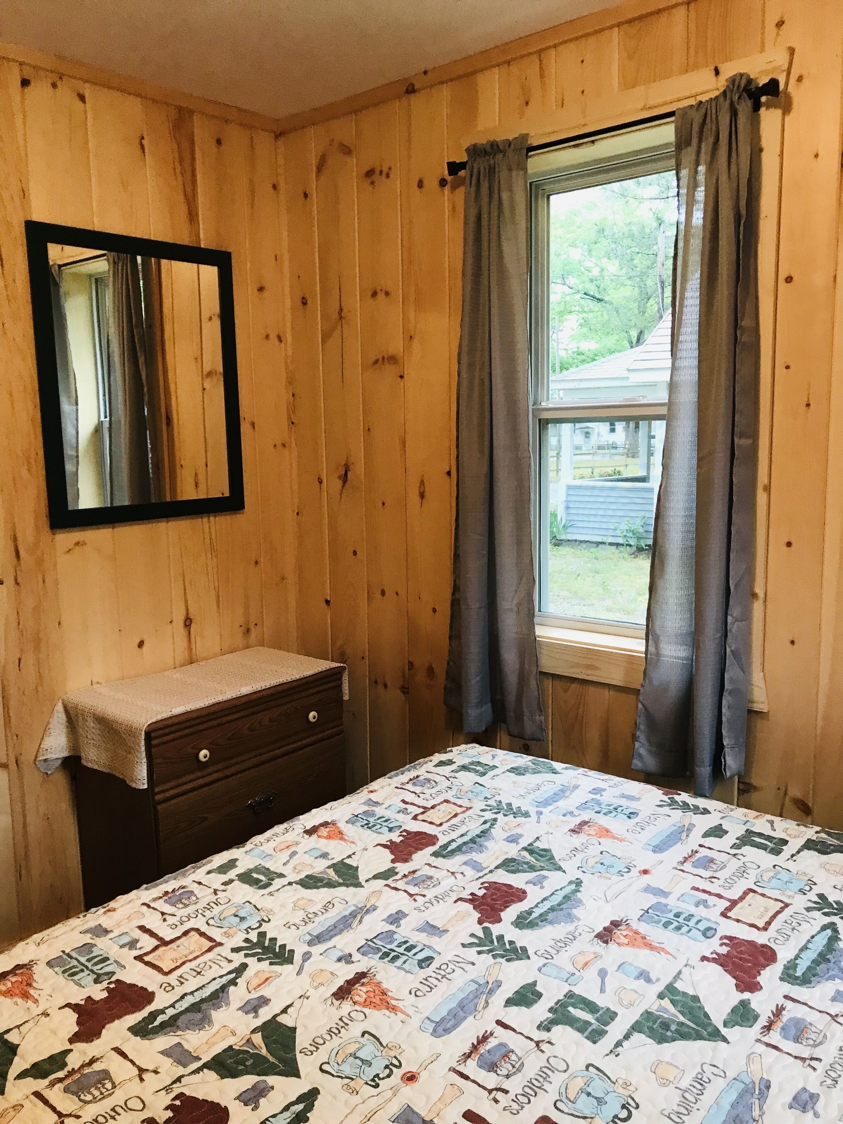 Un dormitorio con paredes de madera, una cama con colcha colorida, un tocador, un espejo y una ventana con cortinas.
