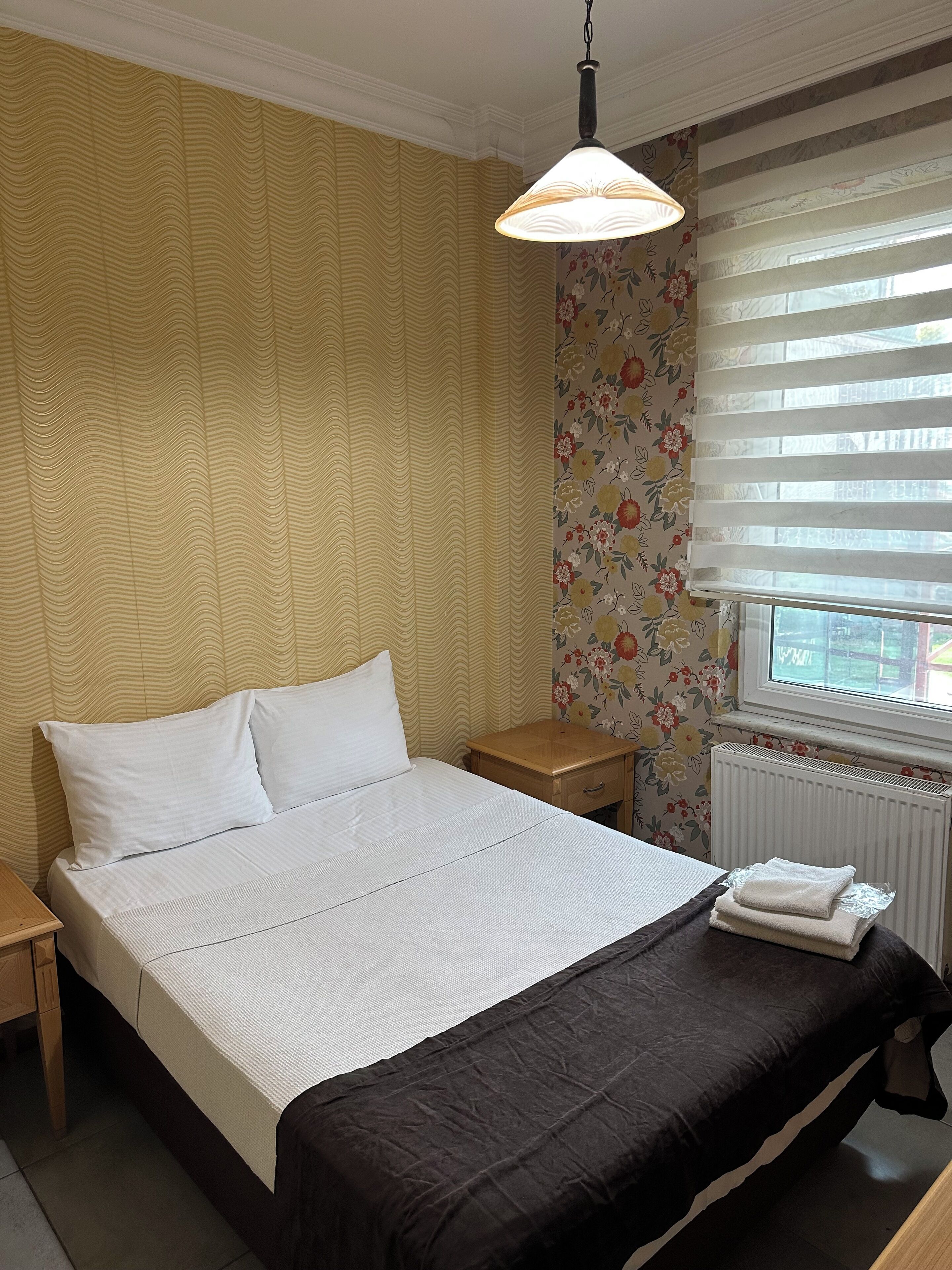 Un lit bien fait, avec du linge de lit blanc, une table de chevet en bois, une petite table et un radiateur.