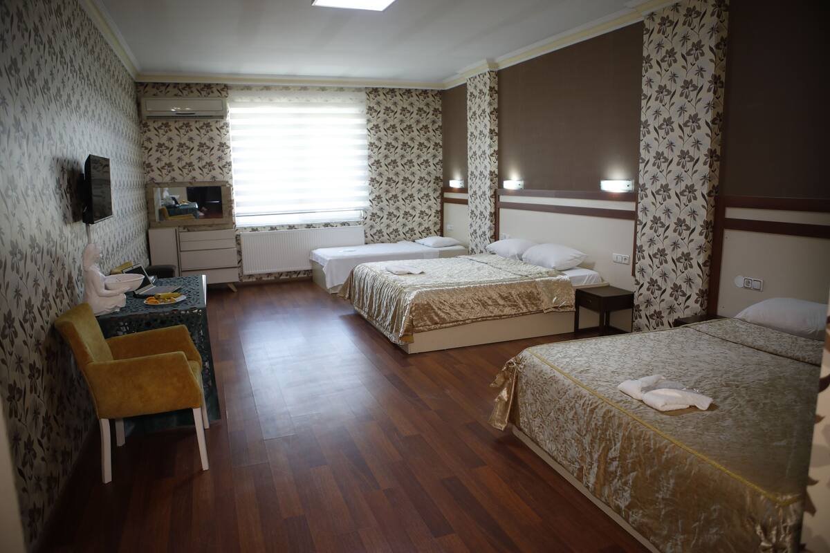 A hotel room with two beds, a desk, a chair, a mirror, and a window with blinds.
