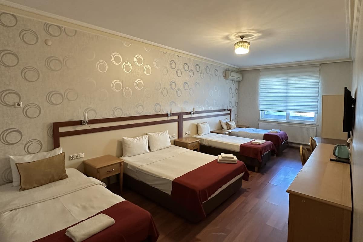 A hotel room with three beds, a desk, and a window with blinds.