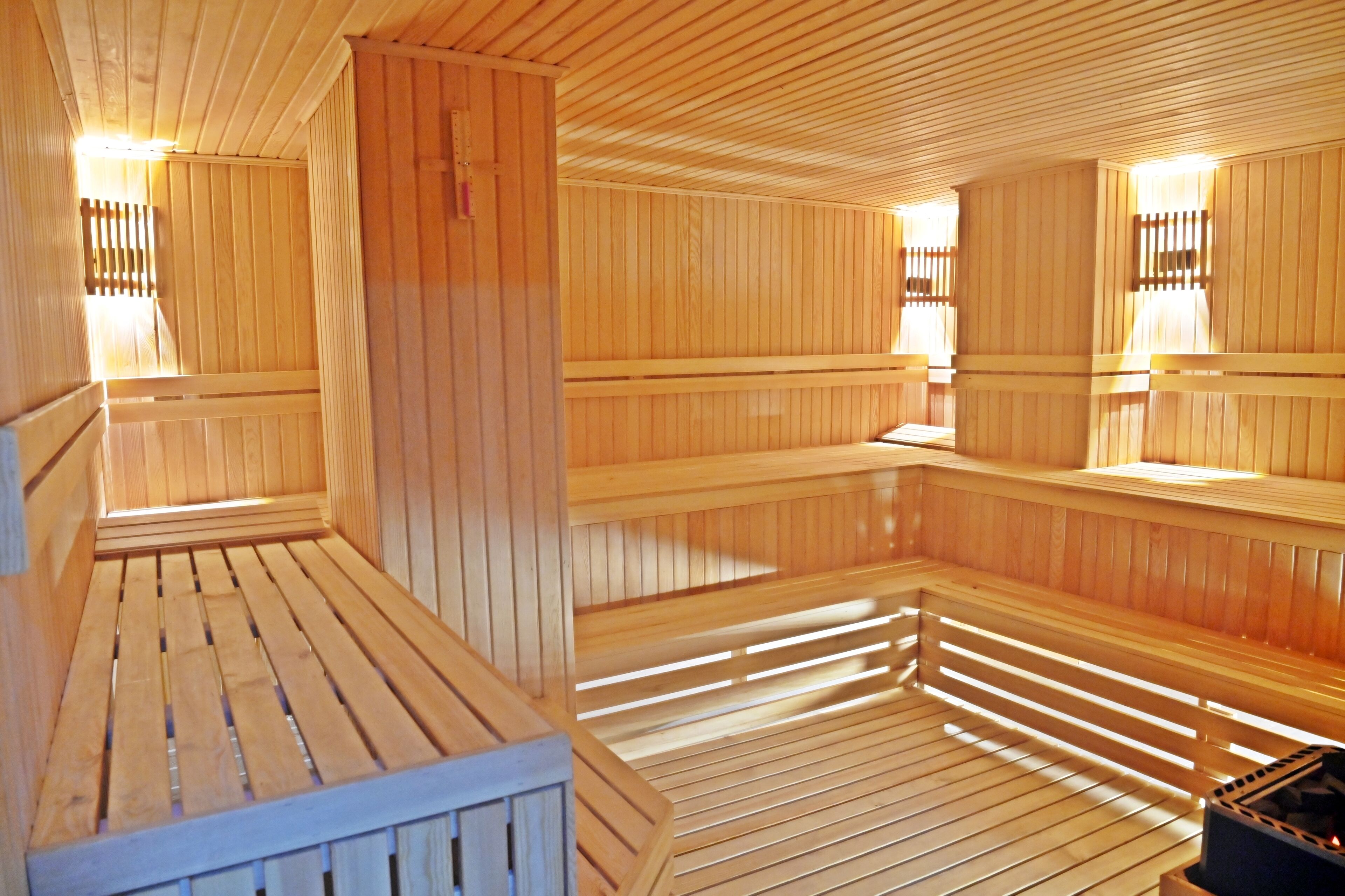Una sauna con bancos y paredes de madera, y un calentador visible en un rincón.