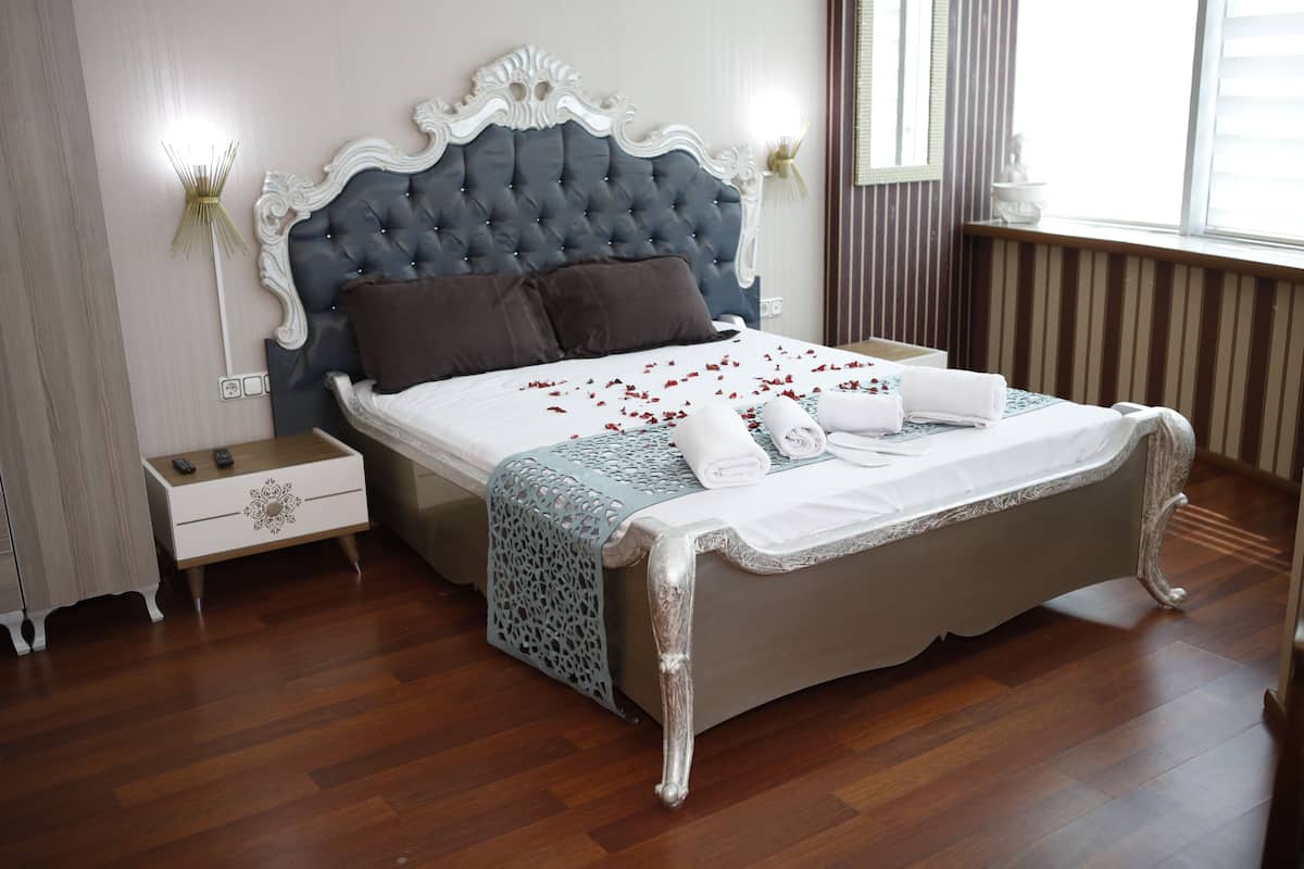 A bedroom with a large bed, a nightstand, a wall-mounted lamp, and a window with blinds.