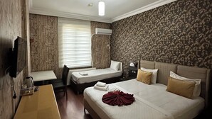 Ein Hotelzimmer mit Bett, Schreibtisch und Stuhl. Es gibt ein Fenster mit Jalousien, eine Klimaanlage und einen an der Wand befestigten Fernseher.
