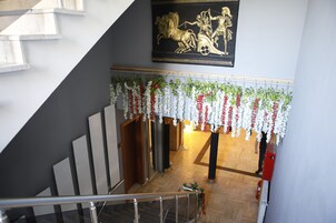 Una escalera con barandilla de metal, un estandarte decorativo con escena clásica y una guirnalda floral colgada arriba.