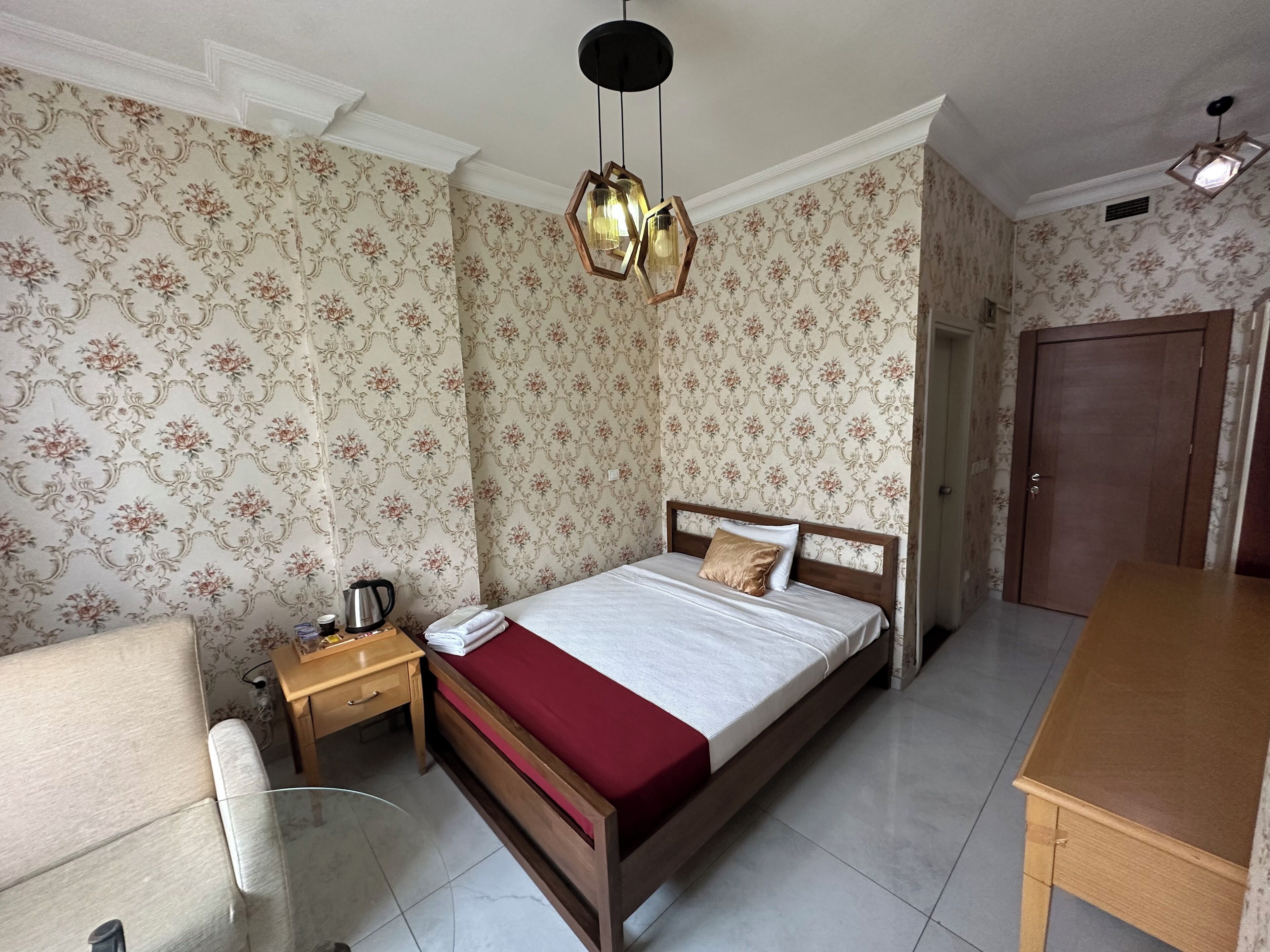 A bedroom with a wooden bed, a nightstand, a chair, a wooden table, and a door.
