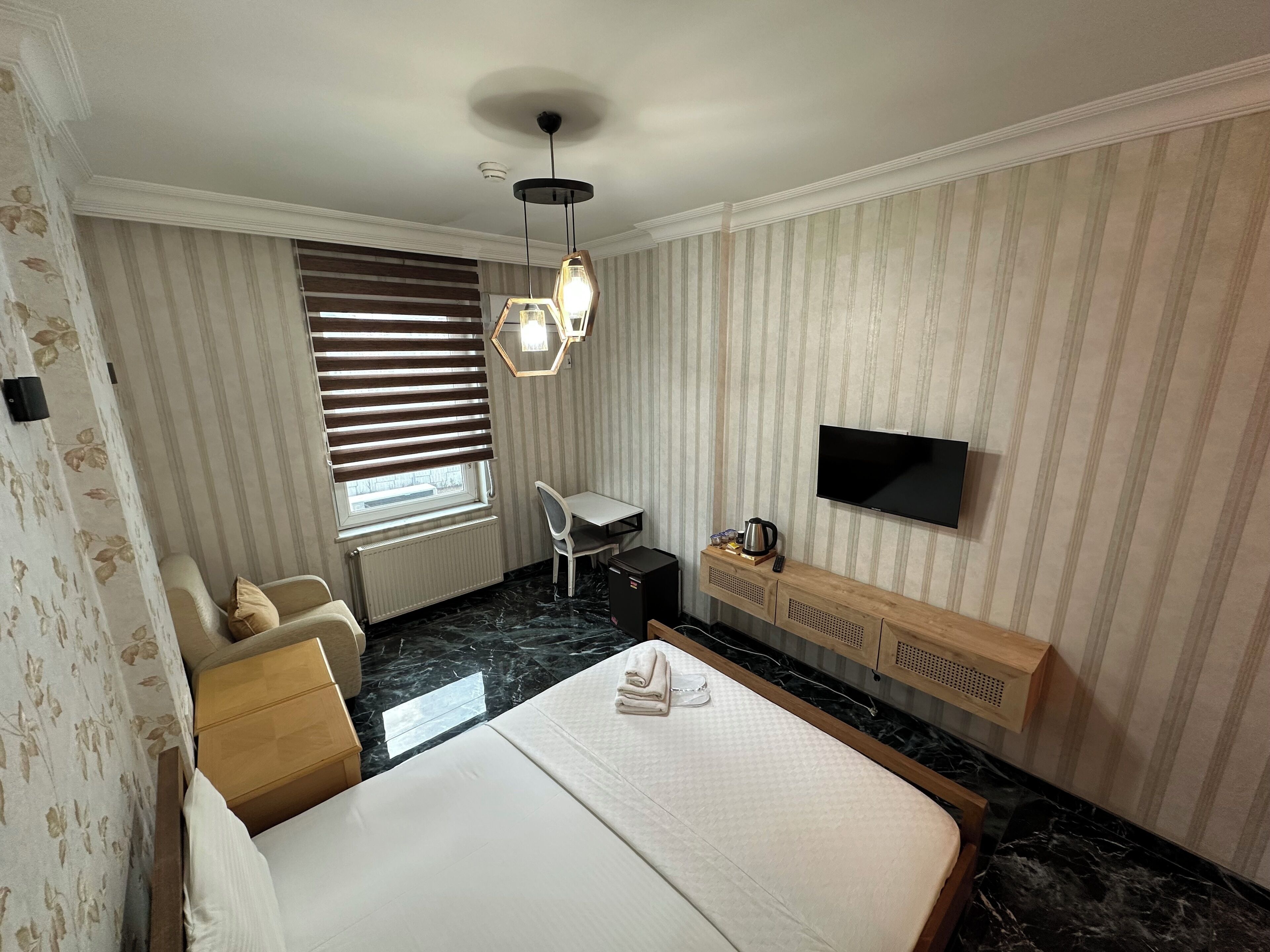 A hotel room with a bed, a desk, a chair, a television, and a window with blinds.