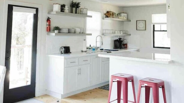 A modern kitchen with white cabinetry, a central island, and two pink stools. - The White Barn (Julian)