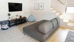 A modern living room with a grey sofa, a flat-screen TV, a staircase, and a small potted plant. - The White Barn (Julian)
