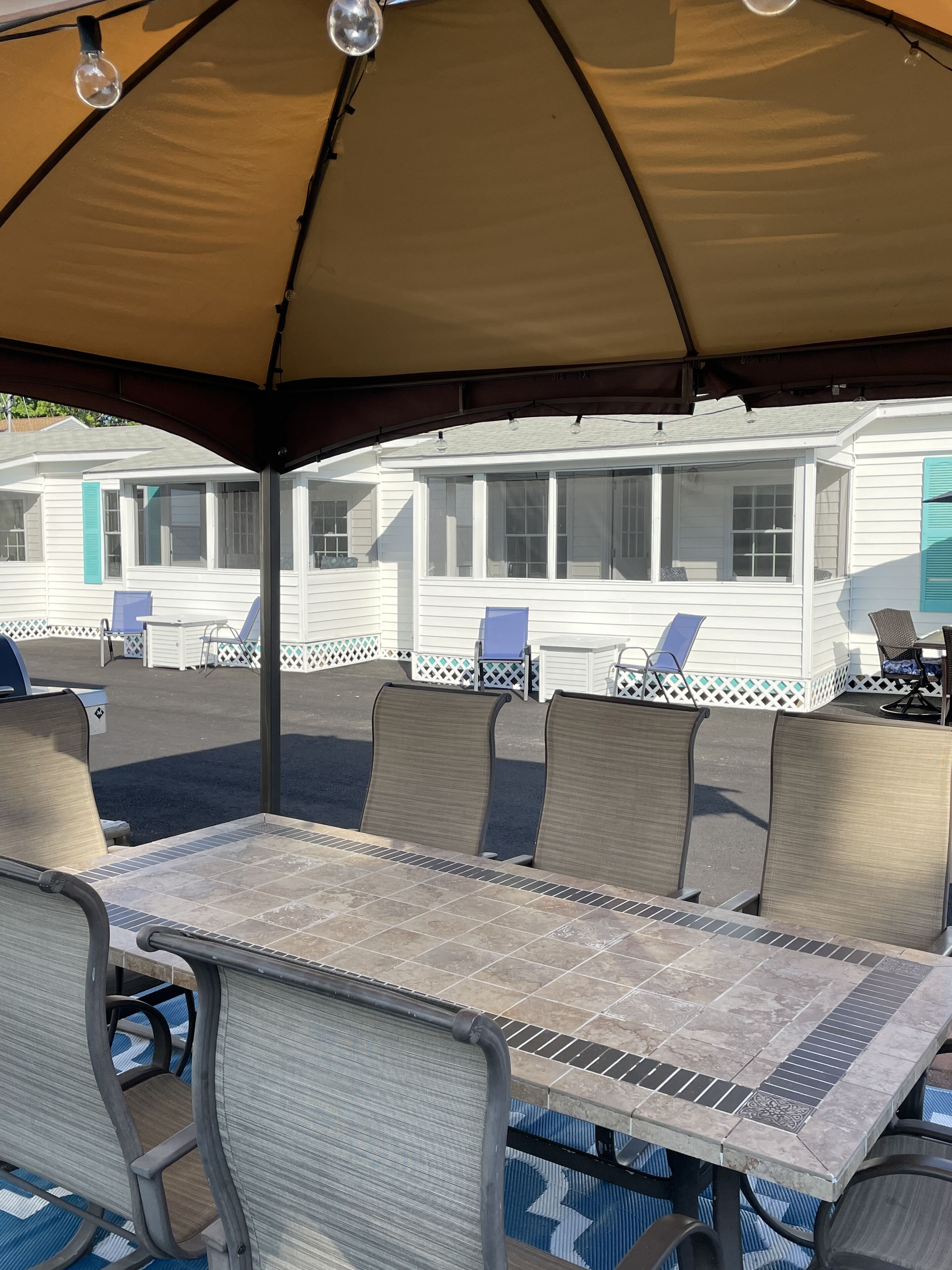 An outdoor patio with a table and chairs, a covered area, and a row of motel rooms in the background.