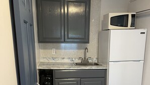 A compact kitchen with dark grey cabinets, a white refrigerator, a microwave, and a stainless steel sink. - Seashell Cottages/JK Rentals - Cottage 1, 2 full beds, 1 twin (Old Orchard Beach)