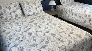 A room with two beds, each with a nautical-themed bedspread, a bedside table with a lamp, and wall art depicting coastal scenes. - Seashell Cottages/JK Rentals - Cottage 1, 2 full beds, 1 twin (Old Orchard Beach)