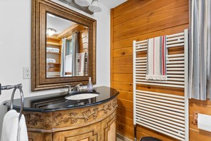 Un baño con tocador de madera, lavamanos, espejo y perchero para toallas.