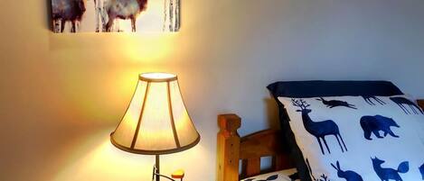 Un dormitorio con cabecera de madera, lámpara de noche, un cuadro de ciervos en la pared y ropa de cama estampada.