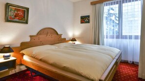 A hotel room with a wooden bed, two bedside tables with lamps, a red patterned carpet, and two framed artworks on the walls. - Chalet Abendrot apARTments by Interhome (Grindelwald)